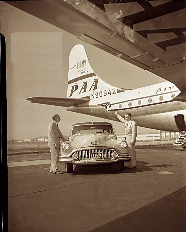 1950s A Pan Am Boeing 377 Stratocruiser serves as a back drop for a vehicle and passengers.